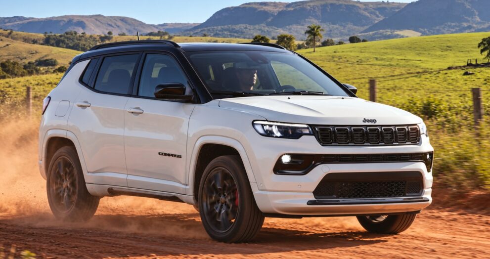 White Jeep Compass SUV with a black roof driving on a red dirt road through green hills